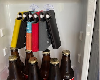 May include: A refrigerator door with six brown glass bottles of beer. The bottles are arranged in two rows of three. The bottles are all different brands. The top of the refrigerator door has five colorful can coolers hanging from suction cups.
