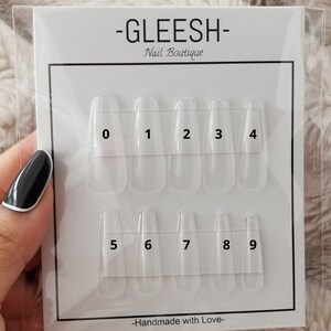 Könnte beinhalten: Ein weißer Kunststoff-Nagelguide mit den Zahlen 0 bis 9, die auf jede Nagelspitze gedruckt sind. Der Guide ist mit "GLEESH- Nail Boutique" und "Handmade with Love" beschriftet.