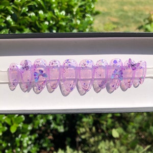 May include: A set of ten purple press-on nails with glitter and butterfly accents.