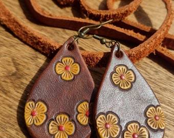 May include: A pair of brown leather earrings with a teardrop shape and a floral design. The flowers are yellow with red centers.