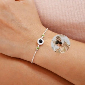 May include: A silver chain bracelet with a black and white photo charm and two green gemstone accents.