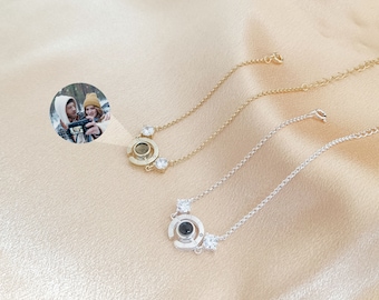 May include: Two silver and gold necklaces with a small round pendant that projects an image when viewed through a small hole. The pendants are adorned with small clear rhinestones.