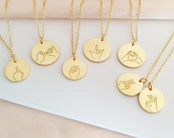 Peut inclure: Ensemble de sept colliers en or avec différents pendentifs en forme de geste de la main. Les pendentifs présentent une variété de gestes de la main, notamment une promesse au petit doigt, un poing, un cœur, un signe de paix, un majeur, des ciseaux et un signe d'accord.
