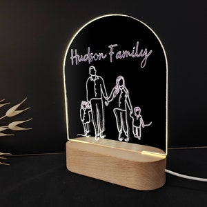 Może przedstawiać: Biała lampka nocna z akrylu z drewnianą podstawą. Lampka przedstawia sylwetkę rodziny czteroosobowej z napisem "Hudson Family" u góry.