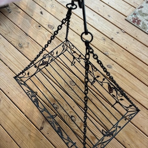 Puede incluir: Estante colgante de metal negro con un diseño floral decorativo. La estantería está suspendida por una cadena.