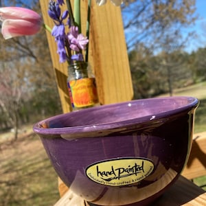 May include: A deep purple ceramic bowl with a glossy finish. The bowl has a gold sticker on the side that reads "hand Painted Individually Hand-crafted & Hand-painted".