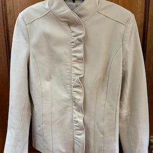 May include: A cream-colored leather jacket with a ruffled front and a stand-up collar.