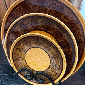 Könnte beinhalten: Drei braune und goldene Keramikteller mit geometrischem Muster, die auf einem schwarzen Metallständer gestapelt sind.