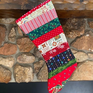 May include: A red and green Christmas stocking with a patchwork design. The stocking is decorated with various patterns, including polka dots, stripes, and snowflakes. The stocking is hanging on a fireplace mantel.