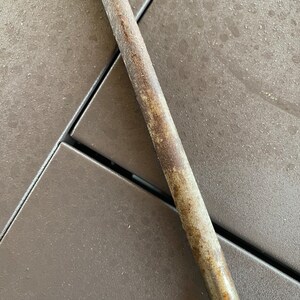 May include: A close-up of a metal file with a rough, textured surface. The file is rusty and has a brown patina. The file is lying on a brown surface.