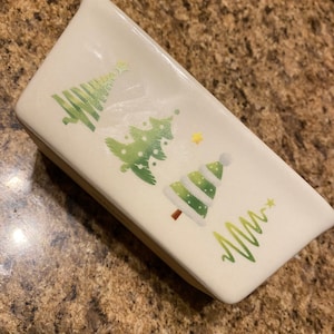 Puede incluir: Un molde para pan de cerámica blanco con un diseño de árbol de Navidad verde y blanco. El molde tiene un diseño festivo con tres árboles de Navidad estilizados y una estrella.