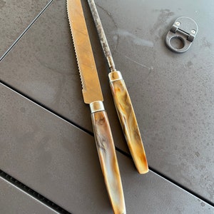 May include: Two kitchen knives with brown and white marbled handles. The knives are on a dark gray surface.