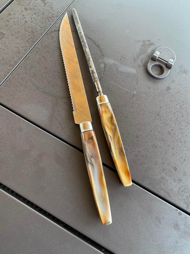 May include: Two kitchen knives with brown and white marbled handles. The knives are on a dark gray surface.