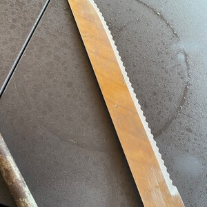 May include: A silver serrated bread knife with a wooden handle lies on a gray surface.