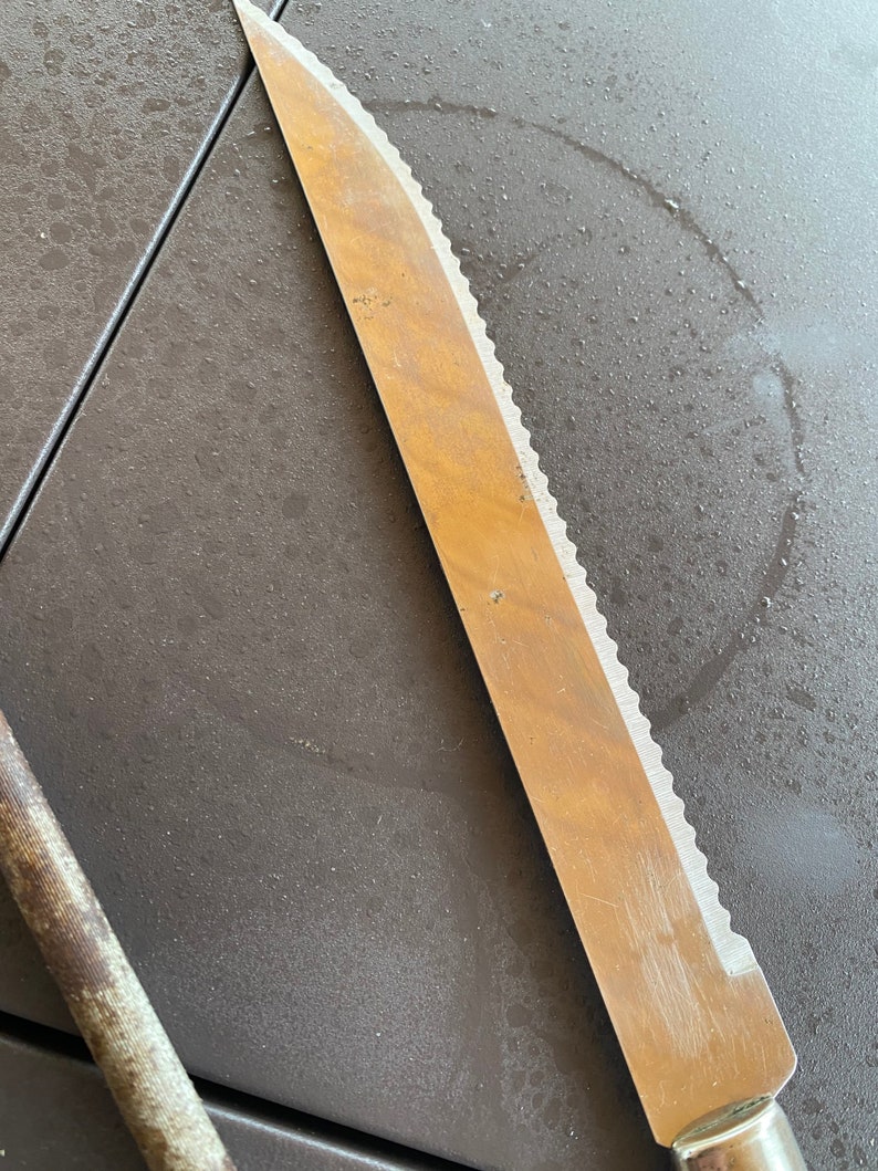 May include: A silver serrated bread knife with a wooden handle lies on a gray surface.