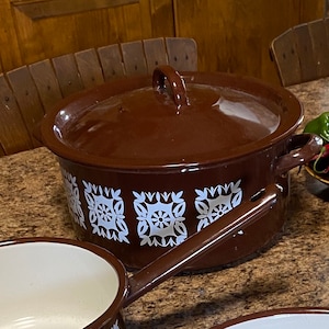 Może przedstawiać: Brązowy garnek emaliowany z białym geometrycznym wzorem. Garnek ma pokrywkę i uchwyt.