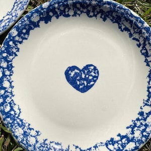 May include: A white ceramic plate with a blue and white speckled border and a blue heart in the centre.