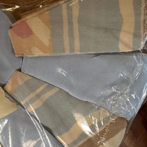 May include: Several fabric face masks are visible, packaged in clear plastic. The masks feature a geometric pattern with stripes in shades of beige, pink, and blue. The masks are folded and appear to be new.