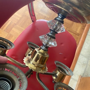 May include: A brass chandelier with four light sockets and a crystal prism hanging from the center. The chandelier is in a vintage style and has a decorative design.