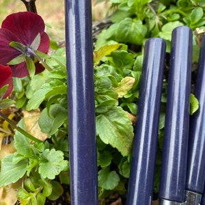 Puede incluir: Cuatro cuchillos de cocina con mangos azules y hojas plateadas. Los cuchillos están dispuestos verticalmente y están enfocados. El fondo está desenfocado y muestra follaje verde.