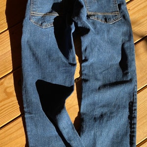 Op de afbeelding: Een donkerblauwe spijkerbroek met lichtbruine stiksels rond de zakken en naden. De broek heeft een ontspannen pasvorm en een rechte pijp.