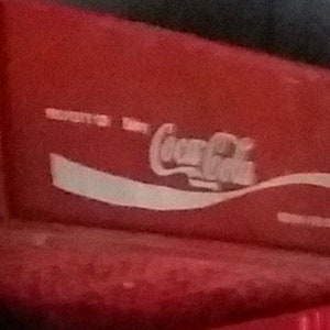 Könnte beinhalten: Eine rote Plastikkiste mit dem Coca-Cola-Logo in Weiß auf der Vorderseite.