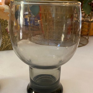 May include: A clear glass goblet with a dark grey base. The goblet has a wide bowl and a thick stem.