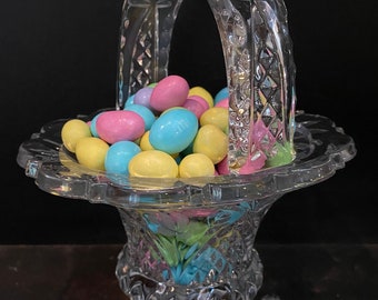 May include: A clear glass candy dish with a handle and three legs. The dish is filled with pastel-colored candy.