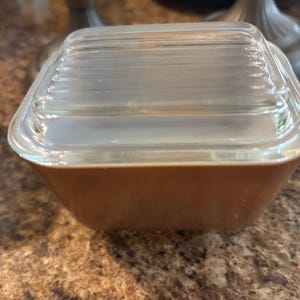 Puede incluir: Un plato para hornear de vidrio marrón con una tapa de vidrio transparente. La tapa tiene un diseño acanalado.