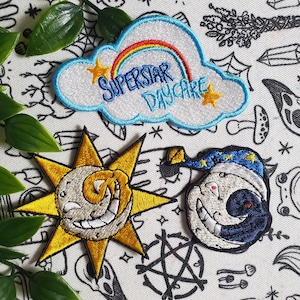 May include: Three embroidered patches featuring a sun, a moon, and a cloud with a rainbow and the text "SUPERSTAR DAYCARE".