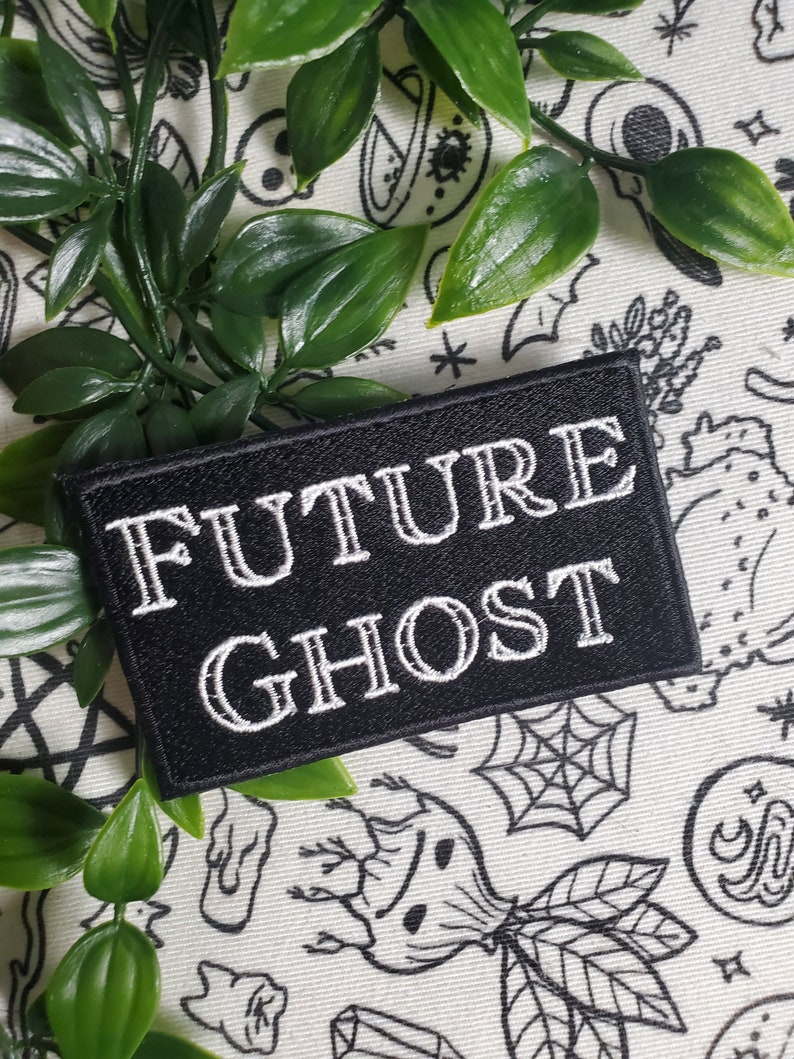 Op de afbeelding: Zwarte geborduurde patch met witte tekst die "FUTURE GHOST" luidt. De patch bevindt zich op een witte achtergrond met zwart-witte illustraties.