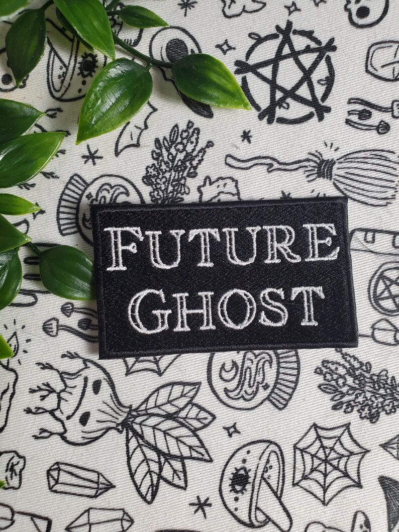 Op de afbeelding: Zwarte geborduurde patch met witte tekst die "FUTURE GHOST" luidt op een witte achtergrond met zwart-witte illustraties van verschillende occulte symbolen.