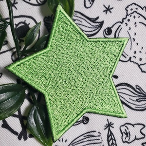 May include: A bright green star-shaped patch with a textured surface. The patch is made of fabric and has a stitched edge.