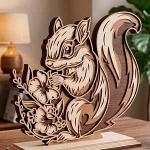 May include: A layered wooden squirrel sculpture with a detailed design. The squirrel is holding flowers and is mounted on a wooden base. The sculpture features various shades of brown and tan, creating a 3D effect. The background includes a lamp and greenery.