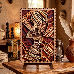 May include: A layered wooden art piece depicting an African woman carrying a vessel on her head. The artwork features geometric patterns in shades of brown, orange, and red, mounted on a wooden easel. The piece is displayed on a wooden table.