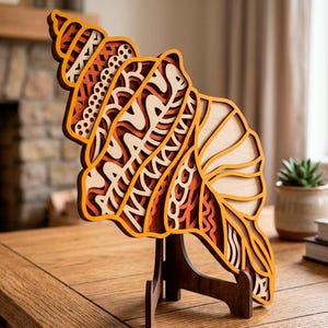 Puede incluir: Escultura de concha marina de madera en capas en tonos naranja, marrón y madera natural. El intrincado diseño presenta varios patrones y texturas, de pie sobre un soporte de madera. La escultura se exhibe sobre una mesa de madera.