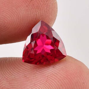 Op de afbeelding: Een levendige rode driehoekige edelsteen met een stervormig patroon in het midden.