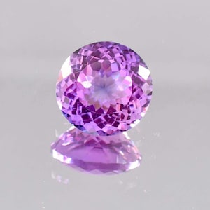 Può includere: Una pietra preziosa di ametista rotonda e sfaccettata con una tonalità viola. La pietra preziosa riflette la luce, creando un effetto scintillante.