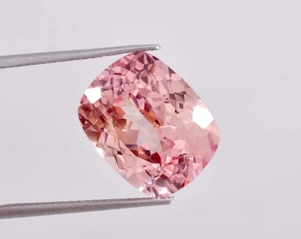 May include: A pink gemstone with a cushion cut, held by tweezers against a white background.