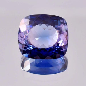 Può includere: Una pietra preziosa a taglio cuscino con un gradiente di colore dal blu scuro al viola. La gemma è sfaccettata e ha un'alta lucidatura.
