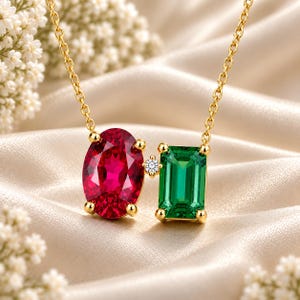 Op de afbeelding: Een gouden ketting met een ovaal geslepen levendig rode edelsteen en een rechthoekige smaragdgeslepen groene edelsteen, verbonden door een kleine, ronde, helderwitte diamant. De stenen zijn gezet in gouden klauwen voor een gebalanceerde hanger.