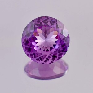 Può includere: Una pietra preziosa di ametista rotonda e sfaccettata con una tonalità viola. La pietra preziosa è tagliata con un motivo a forma di stella al centro.