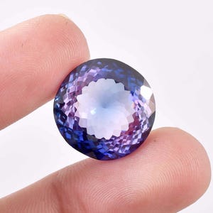 Può includere: Una grande gemma di forma ovale con un gradiente da viola a blu. La gemma ha un taglio sfaccettato e un centro bianco.