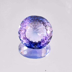 Può includere: Una gemma ovale sfaccettata di colore viola e blu. La gemma riflette la luce e ha un aspetto scintillante.