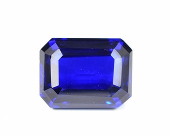 Può includere: Una gemma blu scuro, tagliata a forma rettangolare e sfaccettata. La gemma ha una superficie brillante e riflettente, su sfondo bianco. Il taglio della pietra presenta molteplici sfaccettature che catturano e riflettono la luce, creando un effetto scintillante.