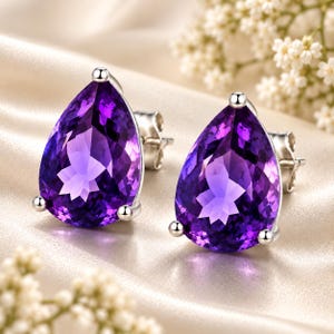 May include: A pair of stud earrings featuring large, pear-shaped, faceted purple amethyst gemstones set in polished silver-toned metal settings with secure post backs, showcasing deep violet hues and clear, reflective surfaces.