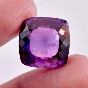 Può includere: Un grande ametista tagliato a cuscino, di colore viola intenso. La pietra preziosa è sfaccettata e ha un alto grado di brillantezza.
