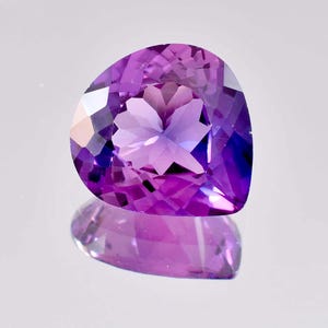 以下が含まれることがあります： ハート型のカットが施された紫色のアメジストの宝石。宝石はファセットカットされており、高い光沢があります。