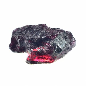May include: A rough, dark red gemstone with a deep, rich color. The gemstone has a natural, unpolished finish and is a beautiful example of a raw crystal.