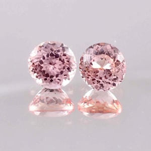 Op de afbeelding: Twee ronde, gefacetteerde, lichtroze edelstenen met een reflecterend oppervlak. De edelstenen hebben een zachte, roze kleur en hun facetten vangen het licht op, waardoor een sprankelend effect ontstaat. De edelstenen zijn waarschijnlijk voor sieraden.